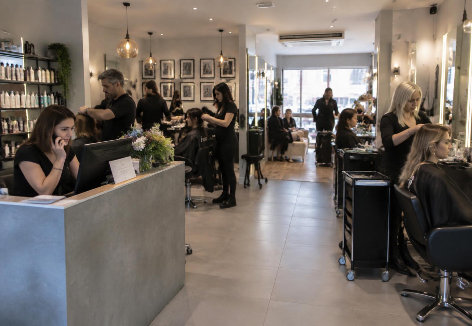 A busy salon with several practitioners serving customers across an active appointment floor.